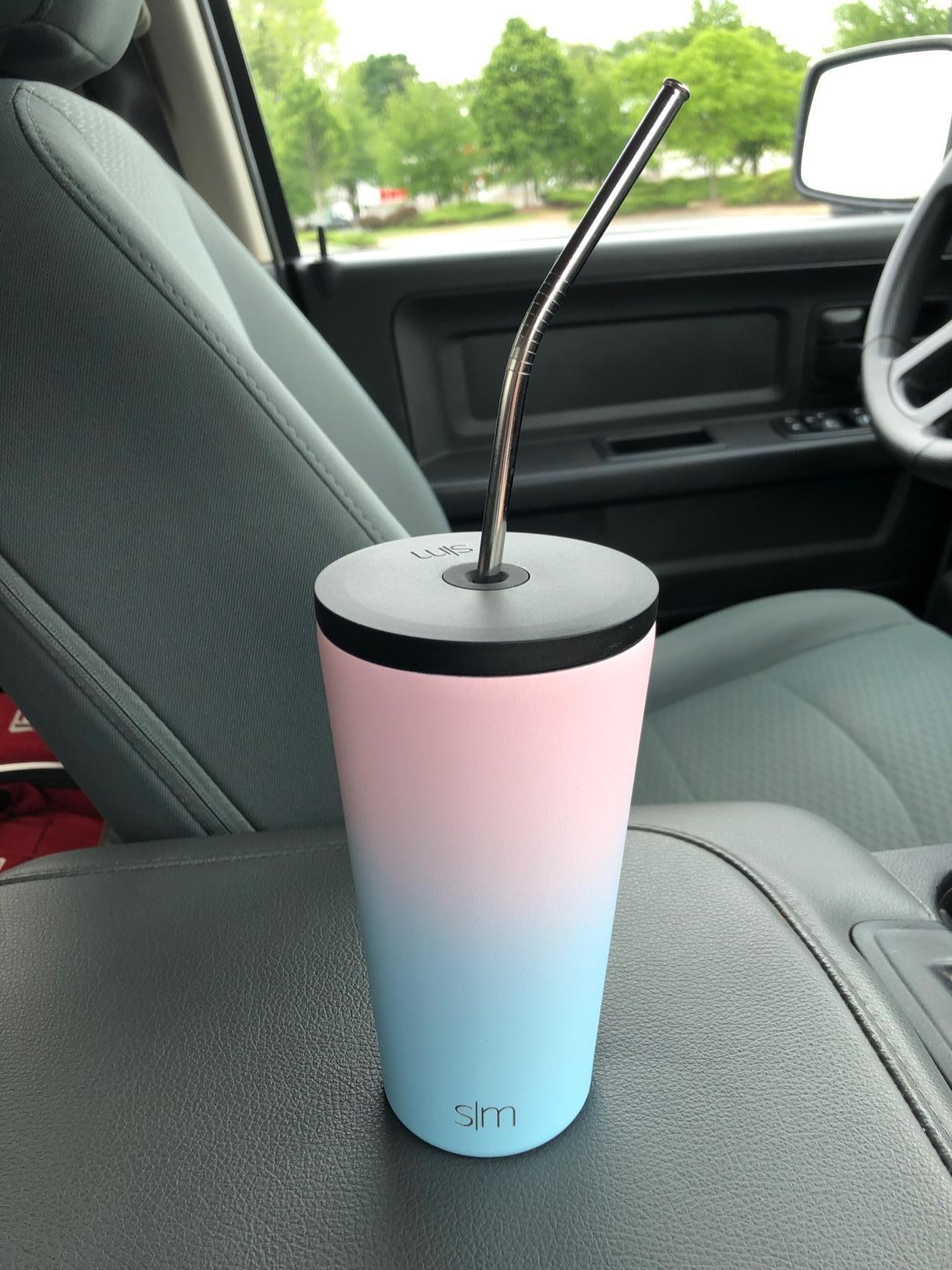 Reviewer&#x27;s photo of blue and pink cup with straw and lid sitting on car console