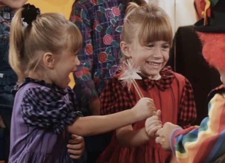 Mary Kate and Ashley smile whilst both holding a wand