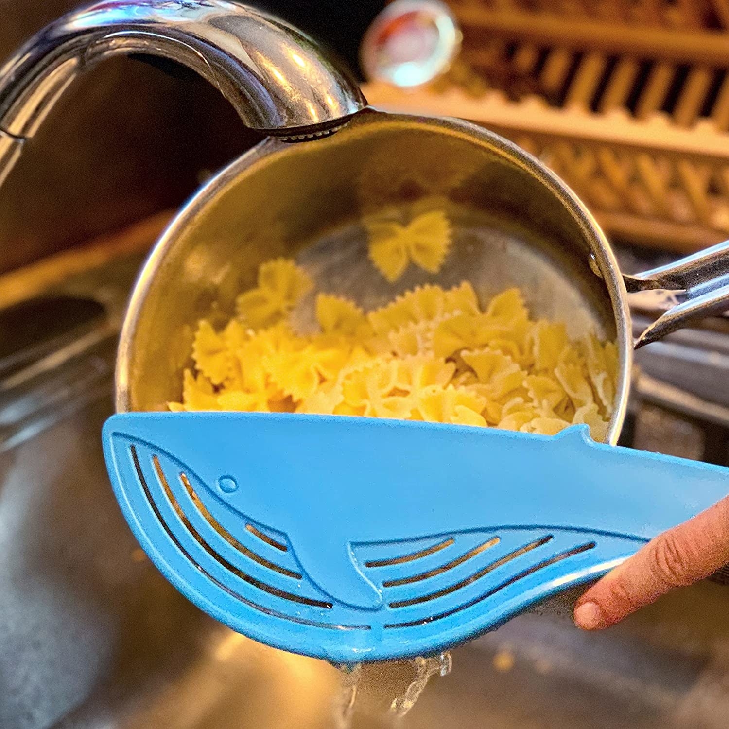 a person using the whale shaped strainer to drain pasta