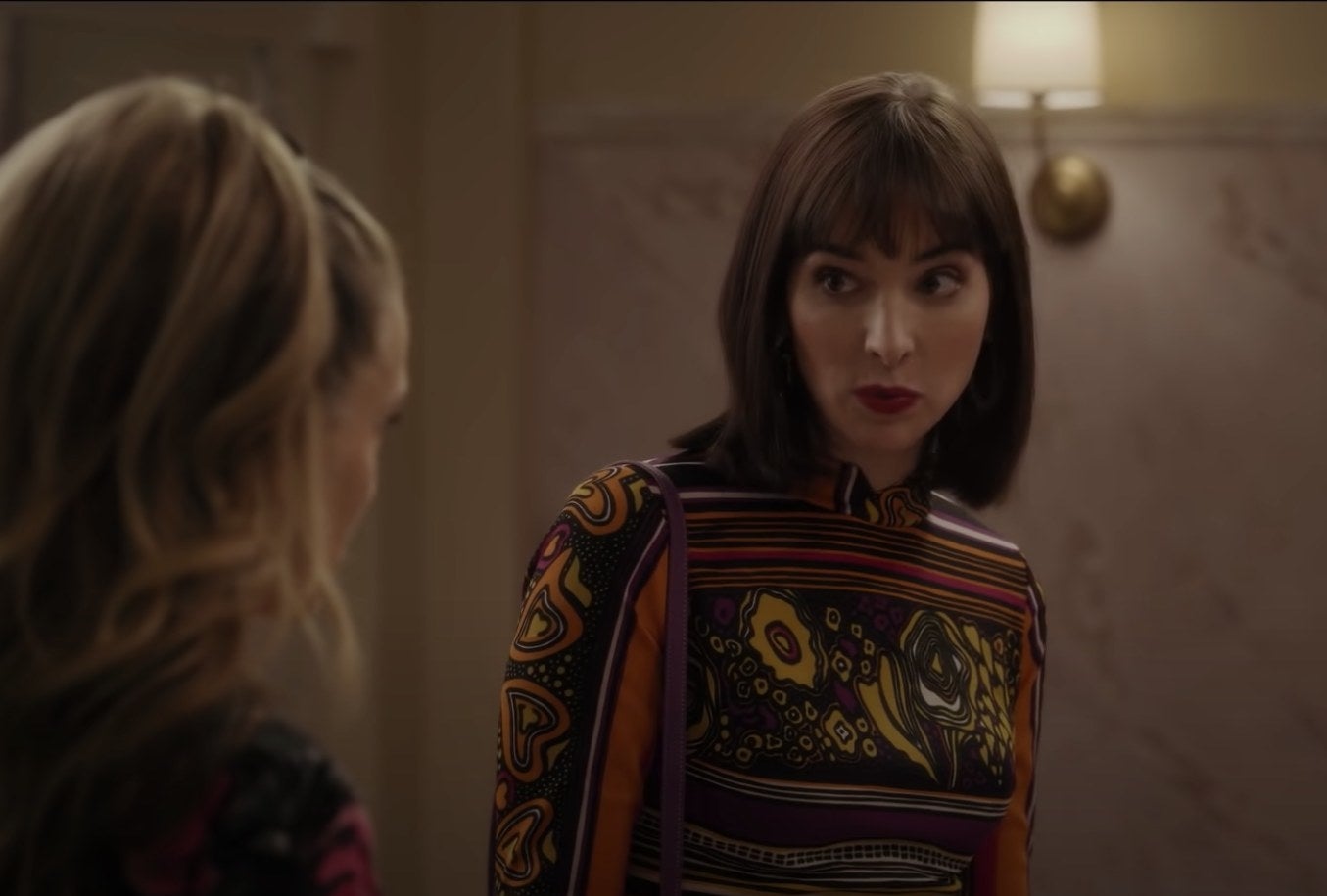 Hari Nef in a formal outfit talking to Sarah Jessica Parker in a bathroom.