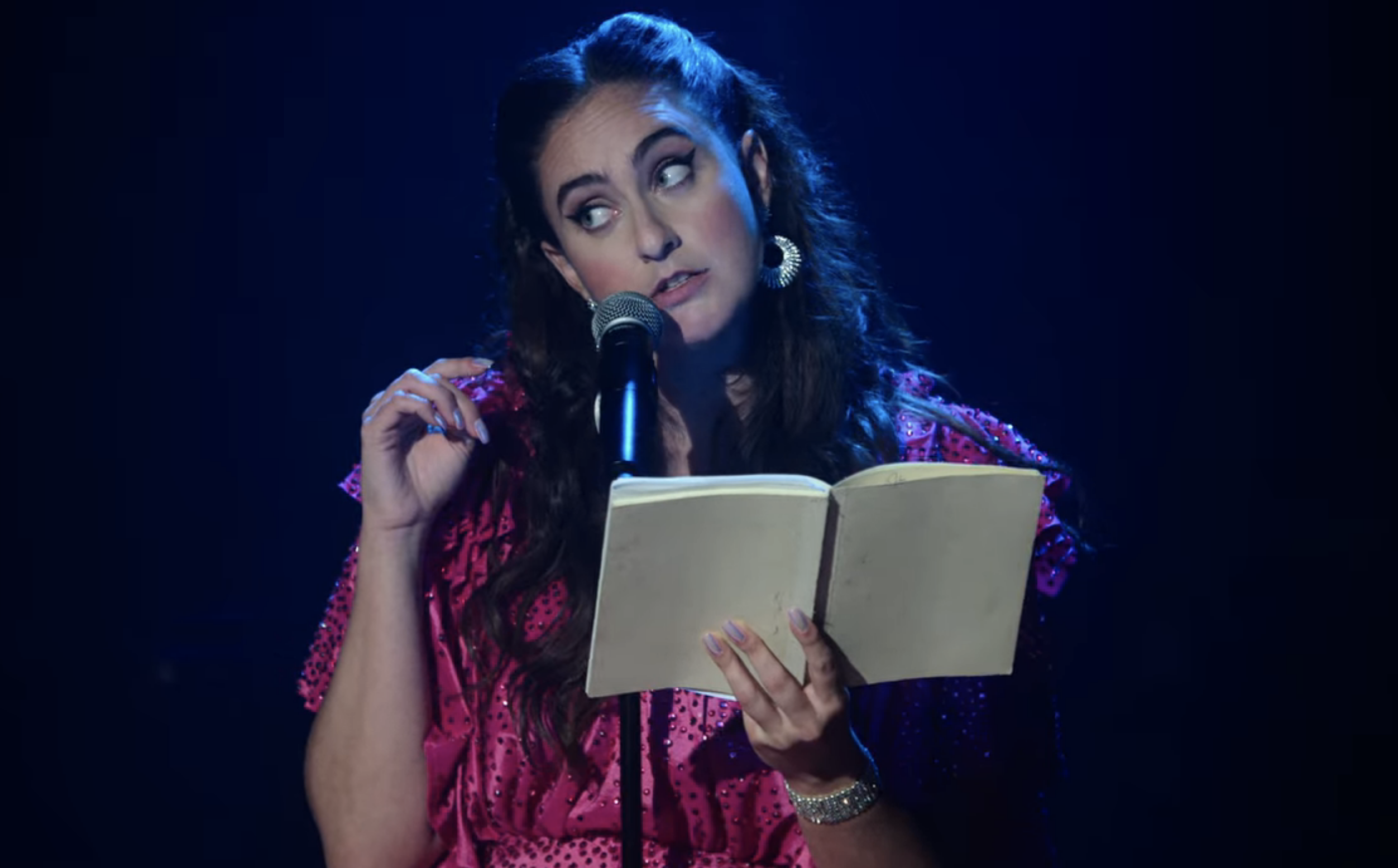 a woman speaking into a mic with a book open
