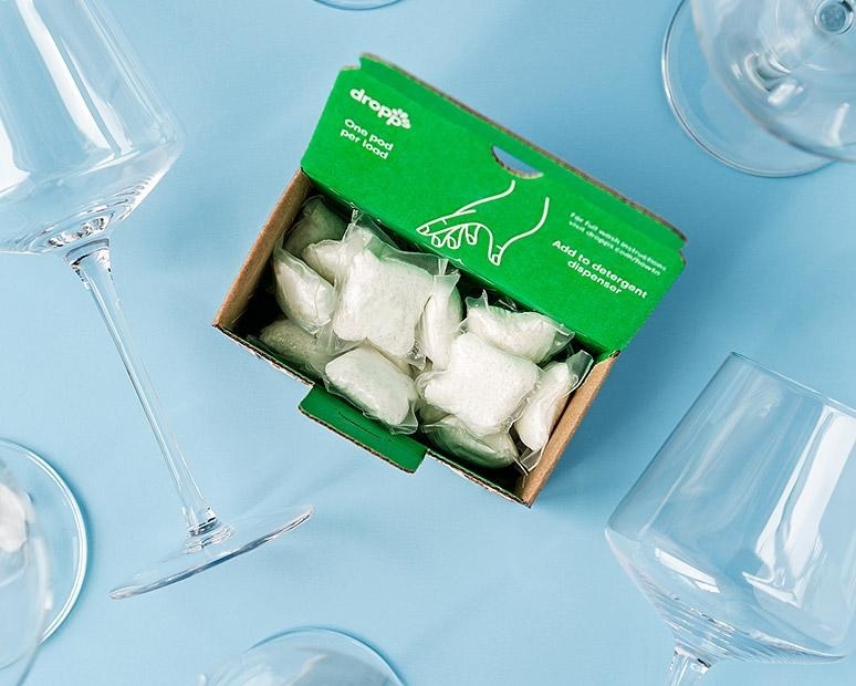 A green box of white detergent pods with glassware