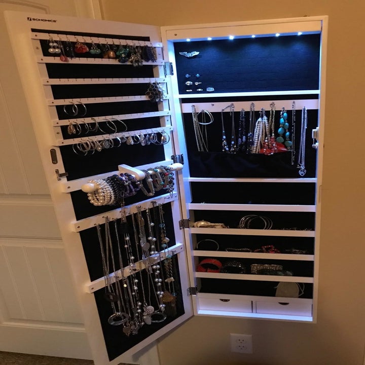 inside a mirror, showing various necklaces, bracelets, and earrings hung with a light turned on at the top