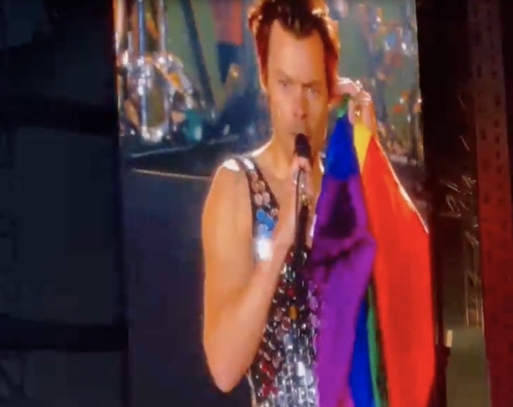 Harry holds a Pride flag by his side on stage