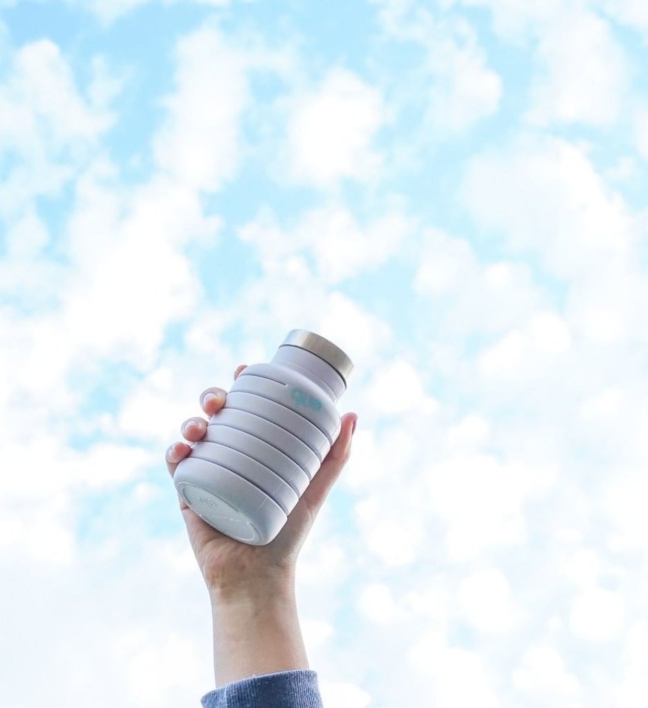someone holding up the foldable bottle against a cloudy sky