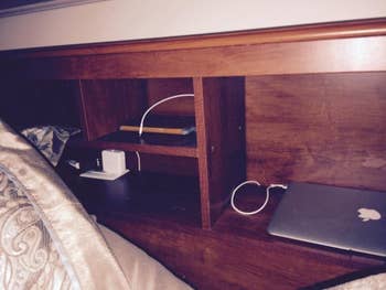 several devices stored in the shelves of the brown wooden storage headboard