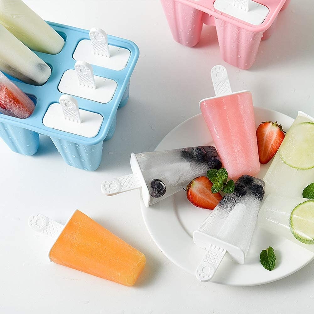 A bunch of popsicles on a plate next to the moulds with more popsicles inside