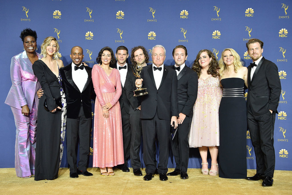 Lorne Michaels holding an Emmy while surrounded by the cast of SNL