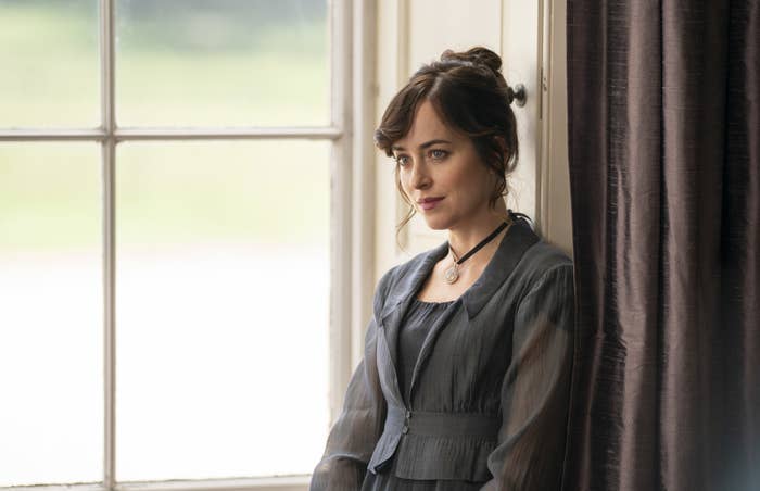 A woman sits at a window looking solemn