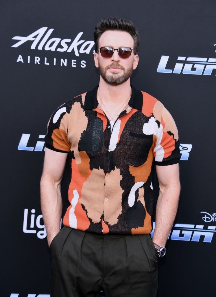 On the red carpet wearing sunglasses and short-sleeved print shirt and with his hands in his pants pockets