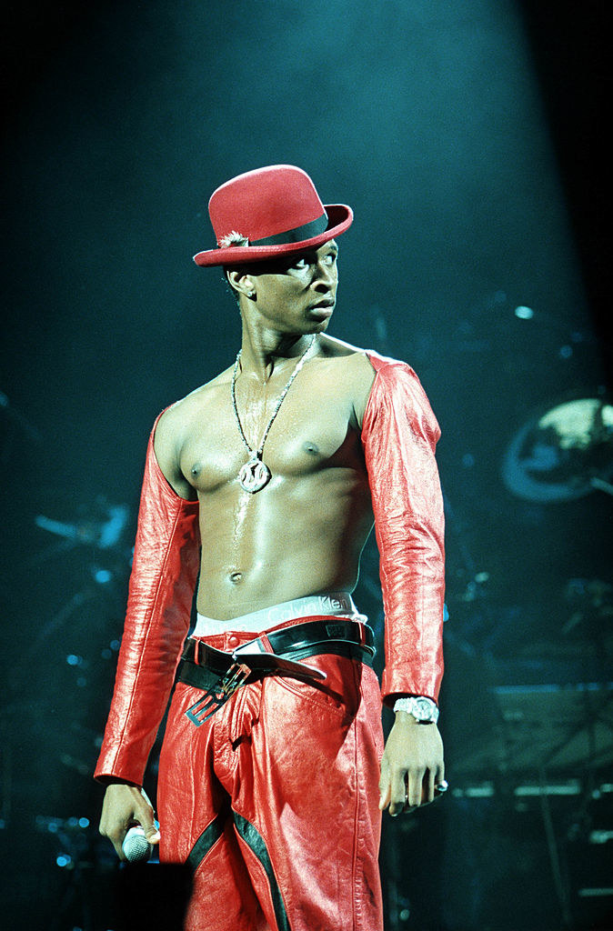 Bare-chested onstage wearing a hat and red leather pants and a top with only sleeves