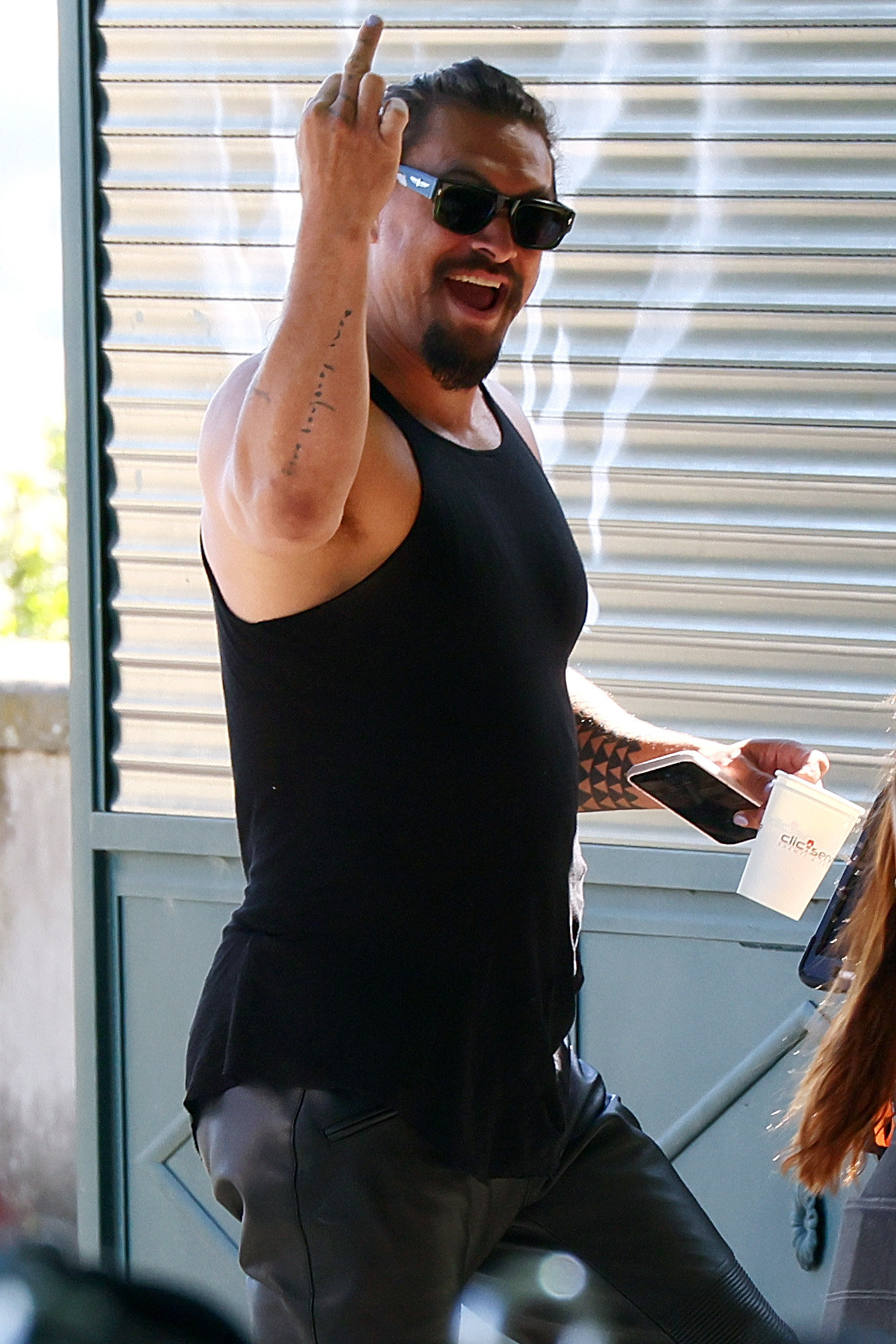 Smiling in a muscle shirt and sunglasses and middle finger raised