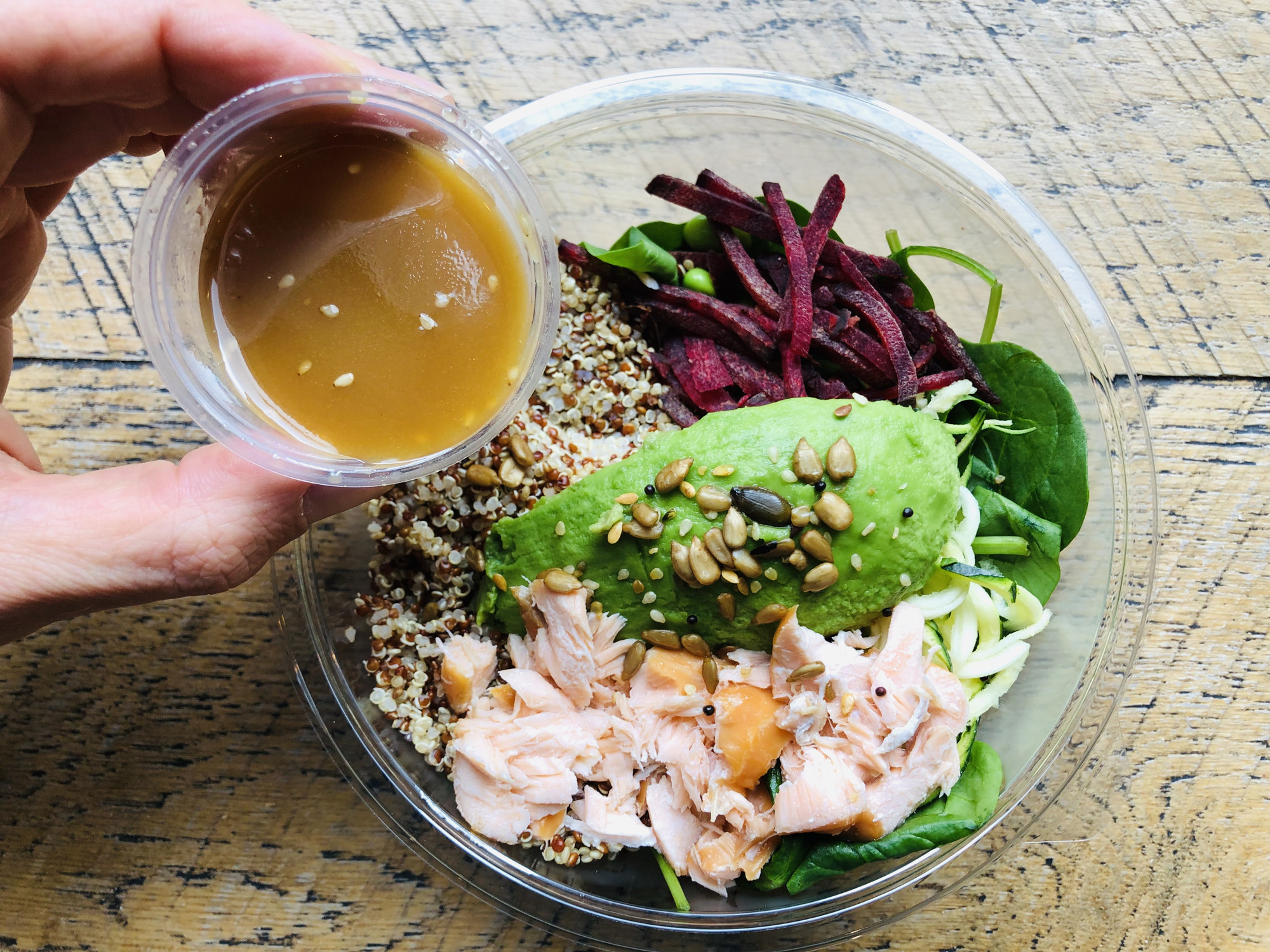 A salmon, avocado, and quinoa salad in a takeout bowl