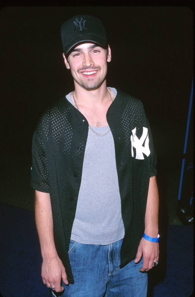 Smiling in jeans and a NY Yankees cap and mesh shirt