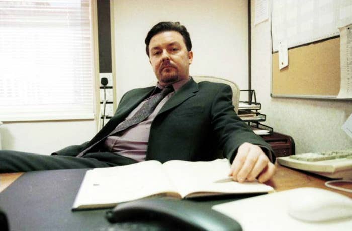 Ricky Gervais sitting at a desk