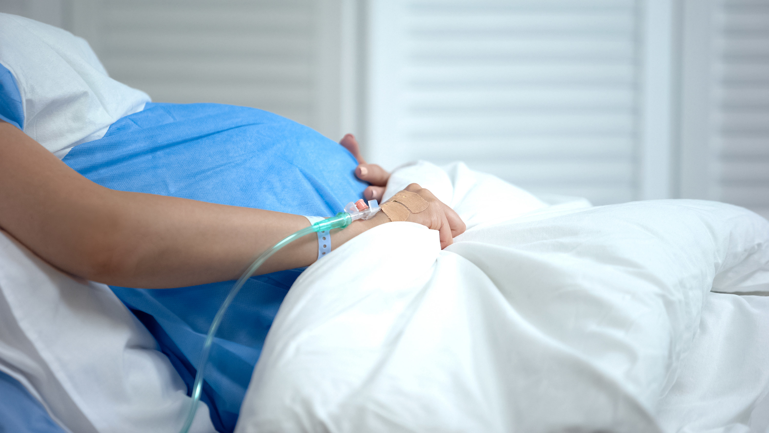 A pregnant person holds their belly in a hospital bed