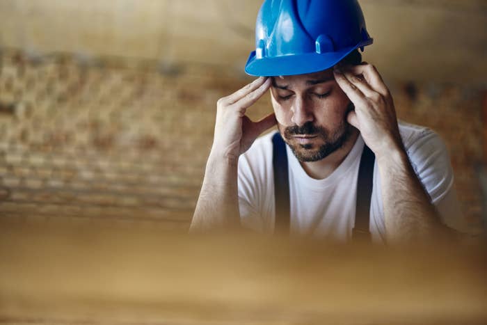 Exhausted construction worker holding his head in pain at construction site