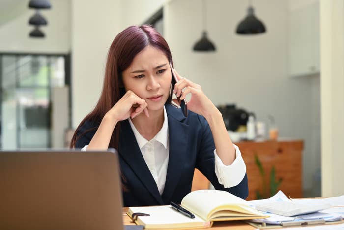 Serious focused female manager sitting in front of laptop and talking on mobile phone, consulting client