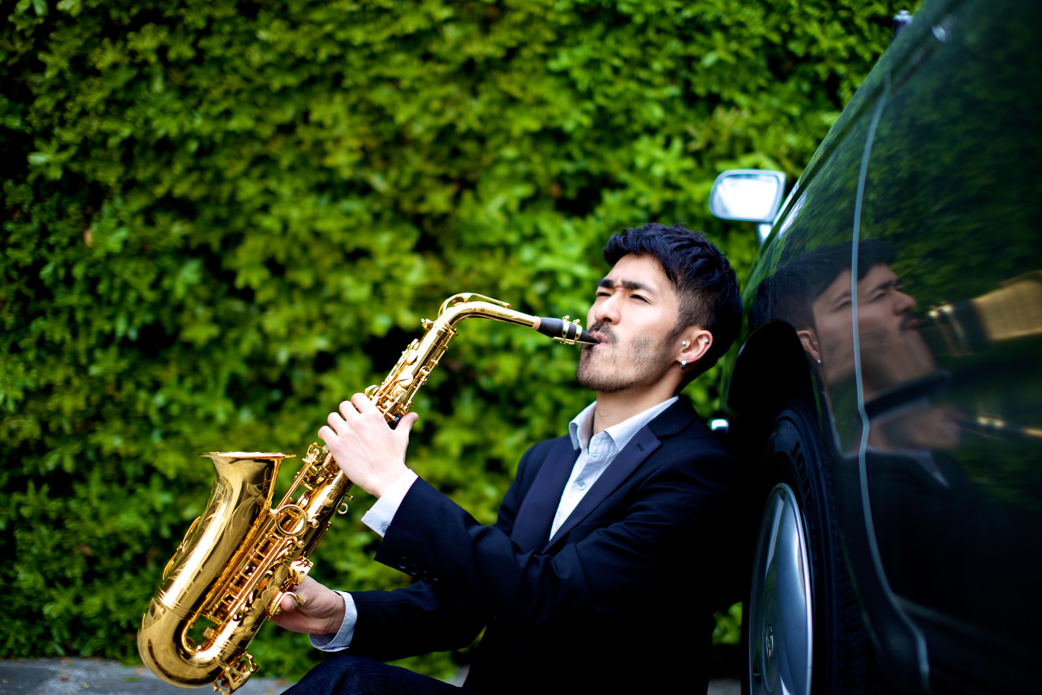 Man playing the saxophone next to a car