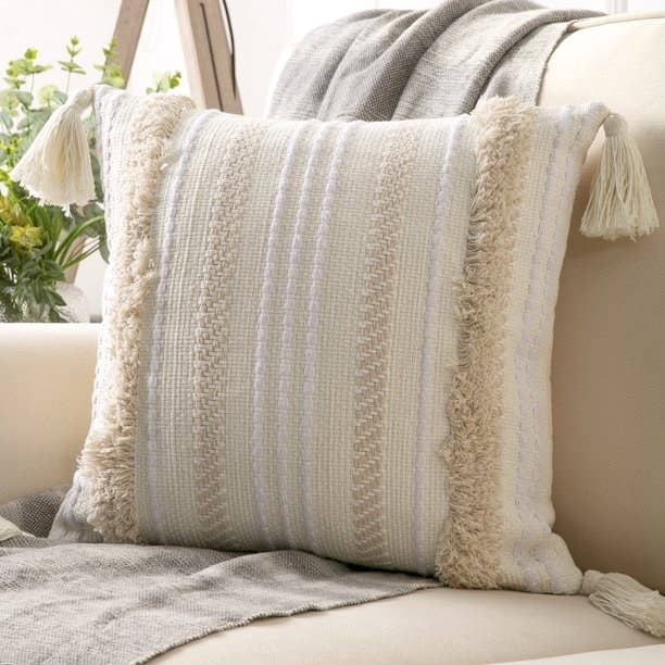 Decorative tasseled pillow on a couch with a textured gray throw blanket