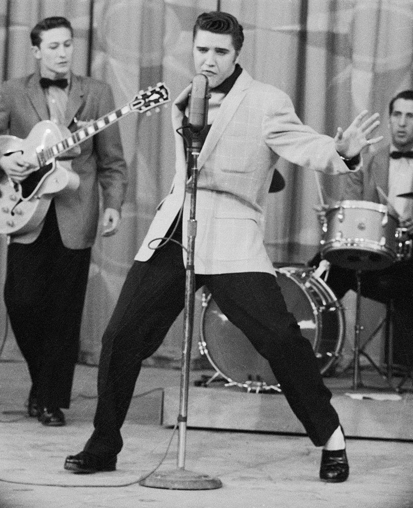 Elvis gyrating in front of a microphone while a band plays behind him