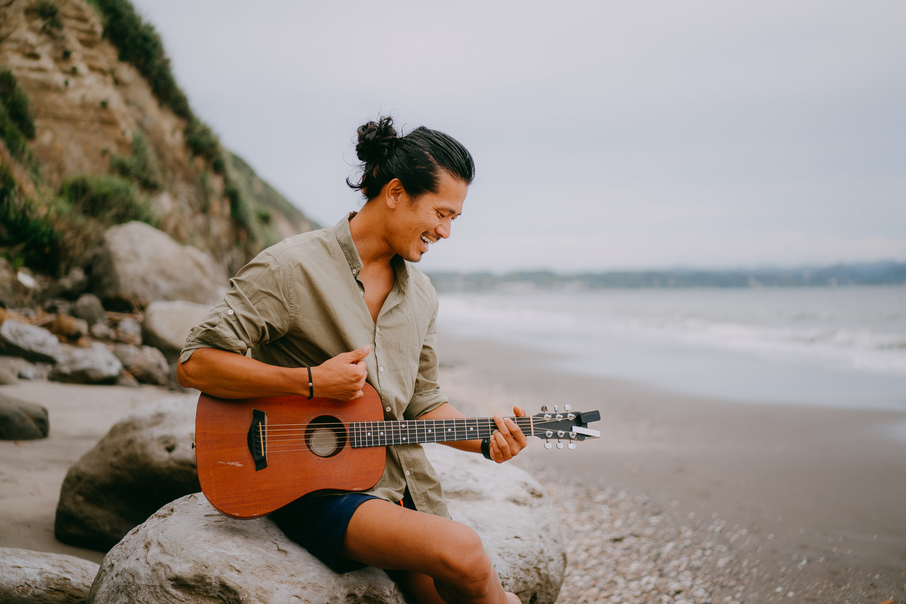 A man smiles as he plays guitar on the beach