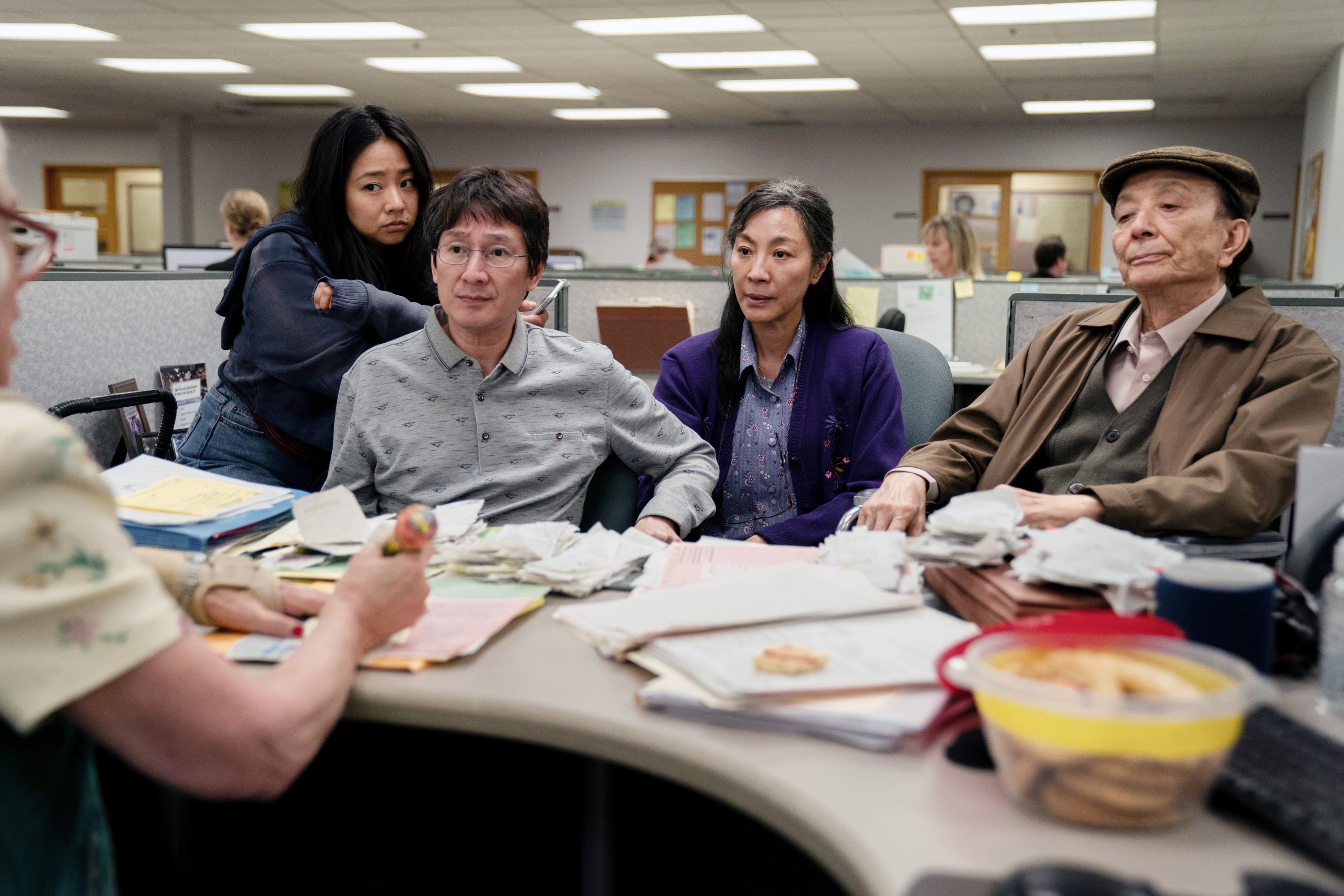 Stephanie Hsu, Ke Huy Quan, Michelle Yeoh, and James Hong sit at a IRS desk