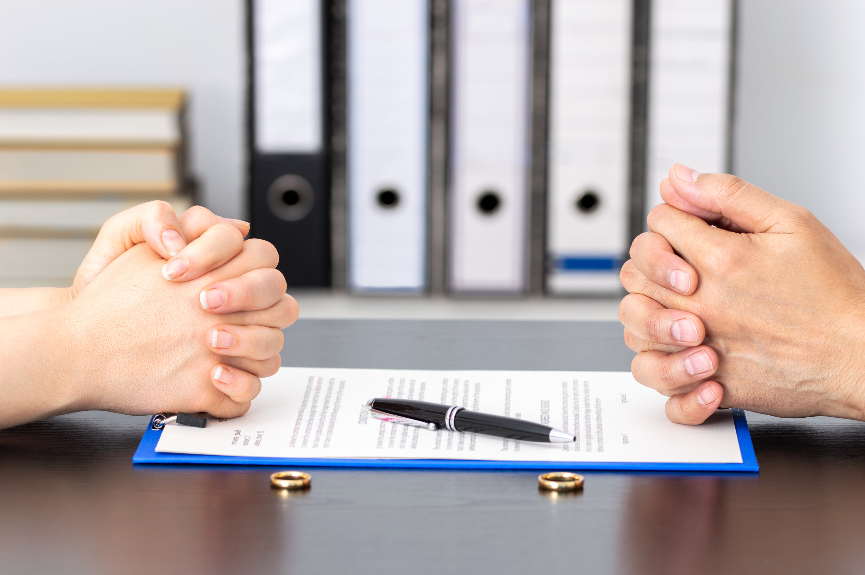 close up of two sets of hands across from each other with wedding rings on the side and paperwork in between them