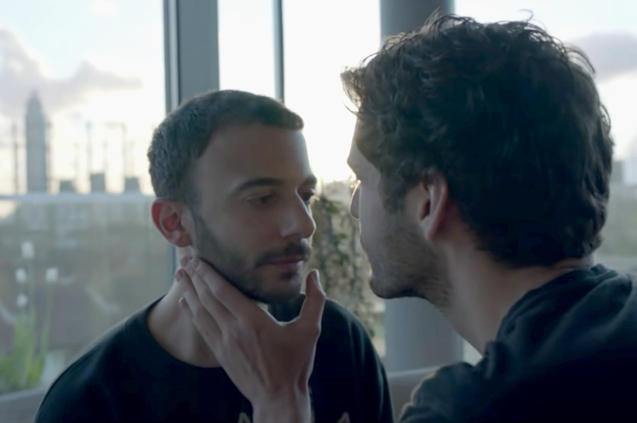 Man puts his hand on another man&#x27;s face lovingly as the sit in a nice London apartment