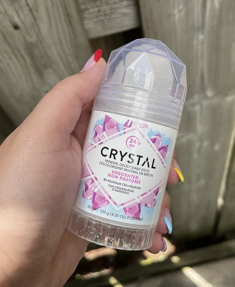 A person's hand holding up the deodorant in front of a fence