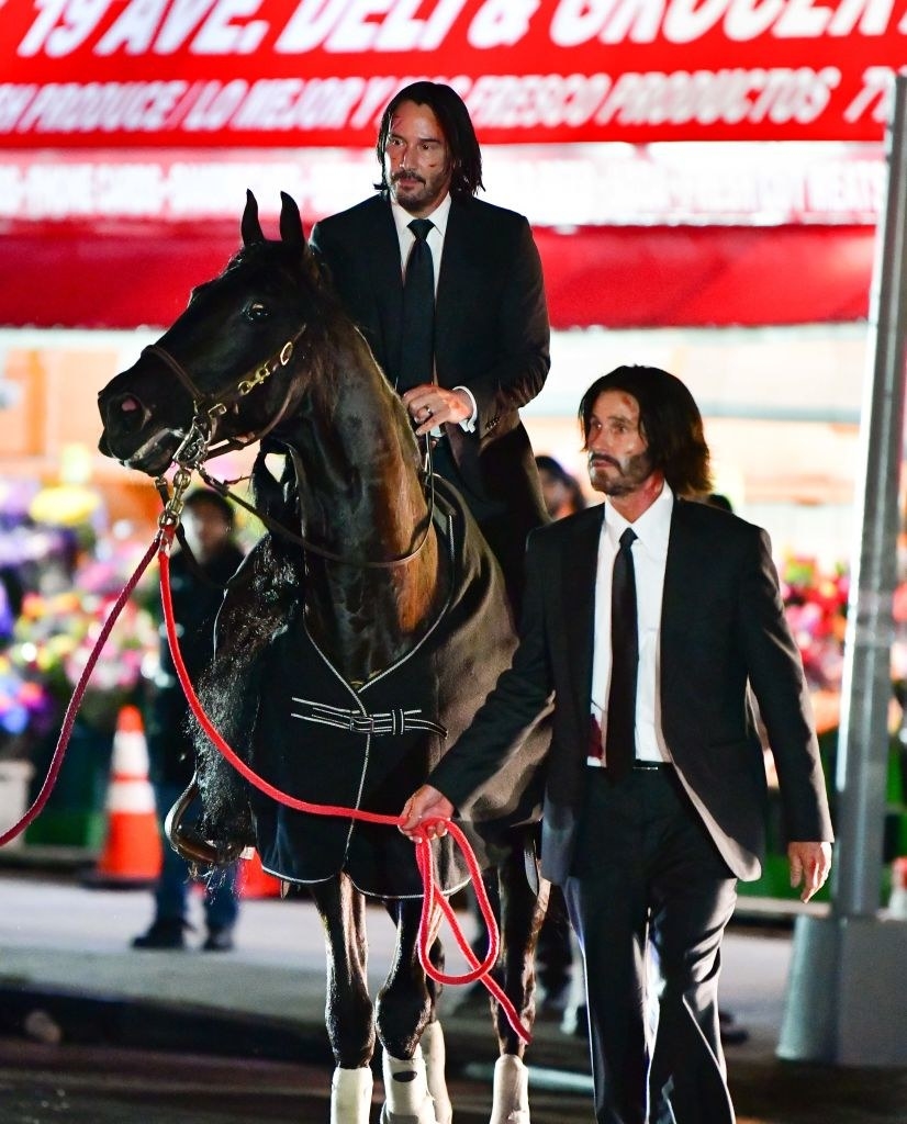 Keanu on a horse with his body double walking beside them and holding the horse&#x27;s rope