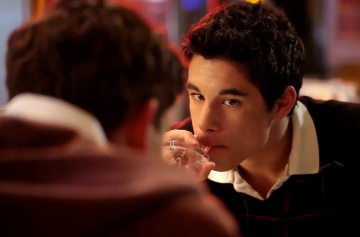 A guy sips a milkshake in a diner provocatively and stares at the guy in front of him who we cannot see