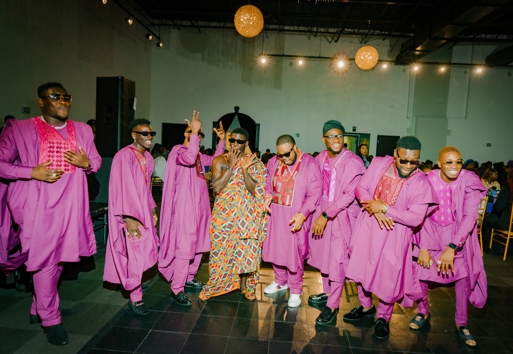 Men wearing purple agbada and kente cloth smile for the camera