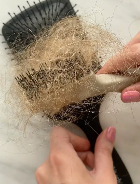 a person using the brush comb to clean out of their paddle brush