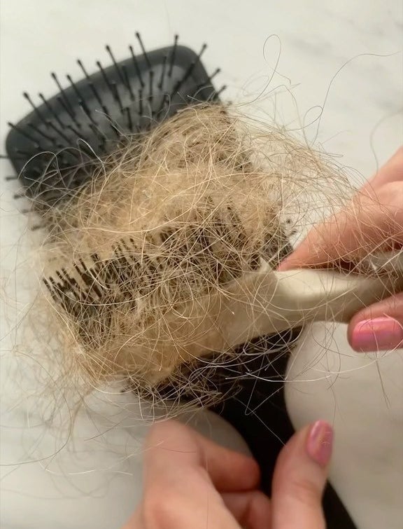 a person using the brush comb to clean out of their paddle brush