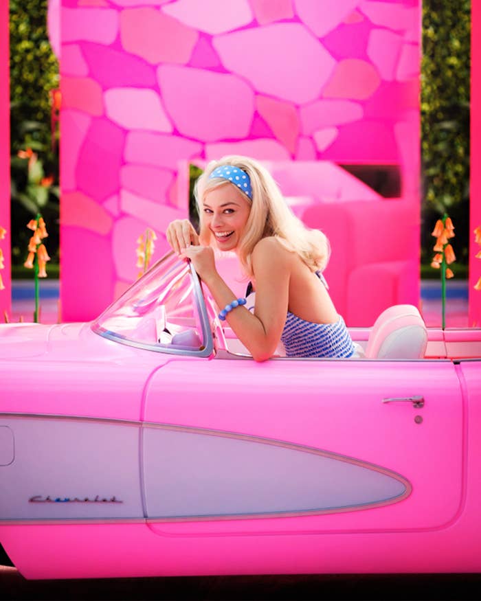 Margot Robbie as Barbie in a 60s mod look and laughing in an open-top convertible