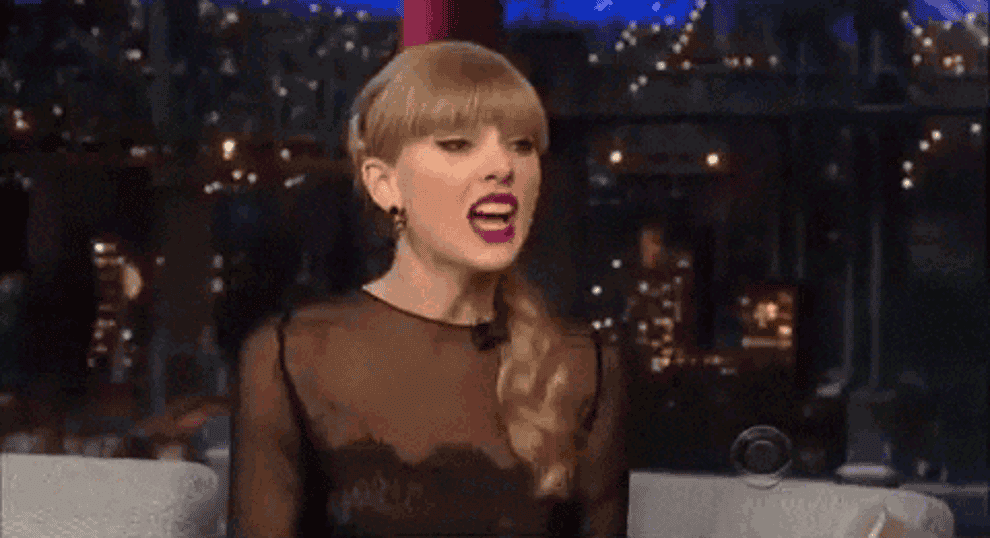 A GIF of Taylor Swift, reacting with hands in the air and her mouth open wide