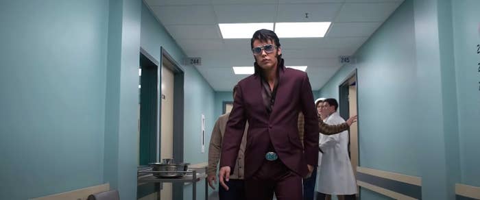 Elvis walking down a hallway in a suit and sunglasses