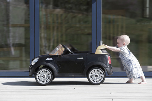 A baby pushes a toy car that&#x27;s bigger than they are