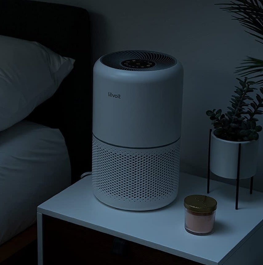 the air purifier on a nightstand next to a bed