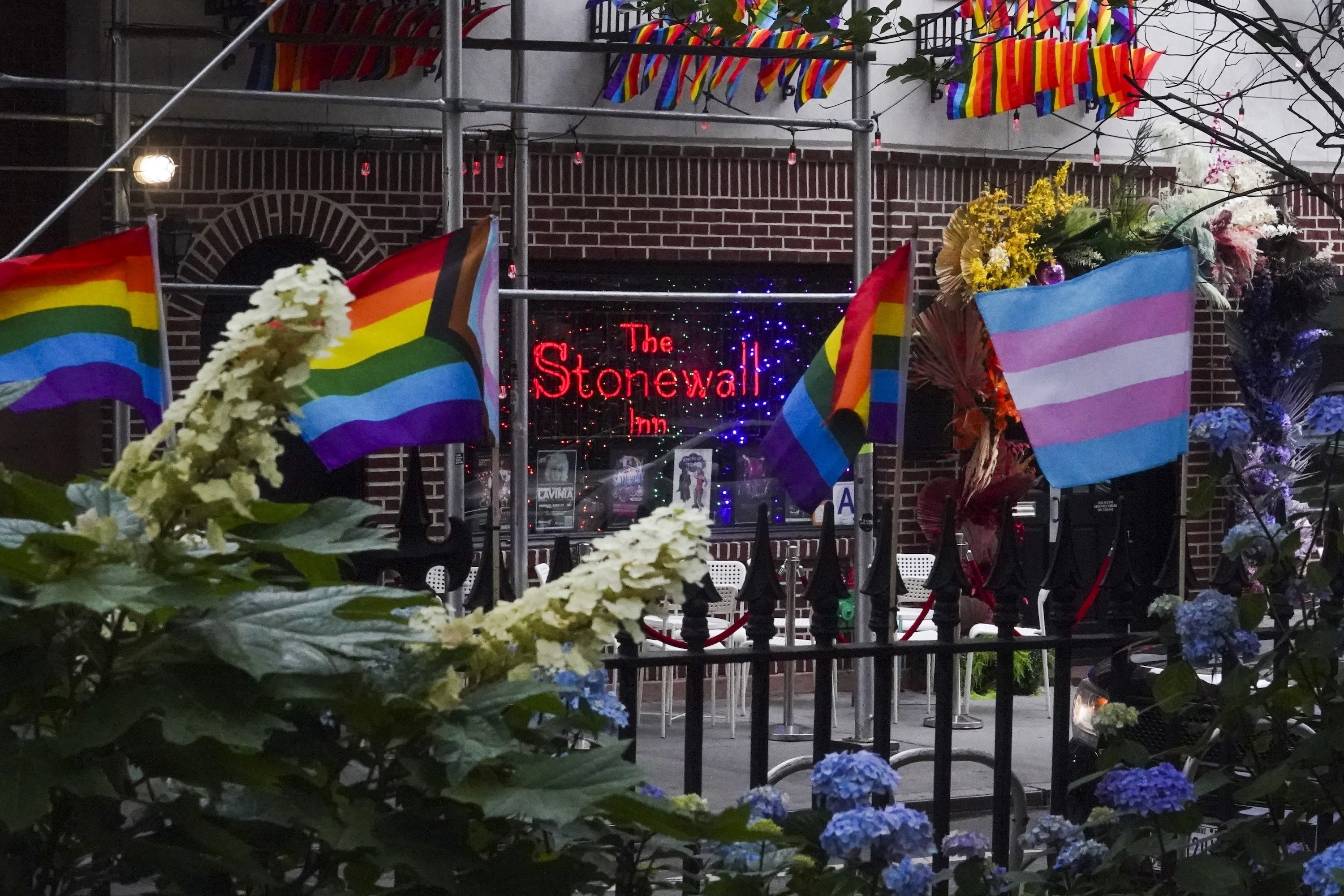 The Stonewall Inn sign appears in the front window with Pride flags in front of it by a gate