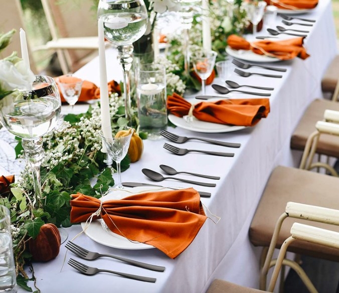 Matte black silverware used on a table set with greenery, white candles and orange accents