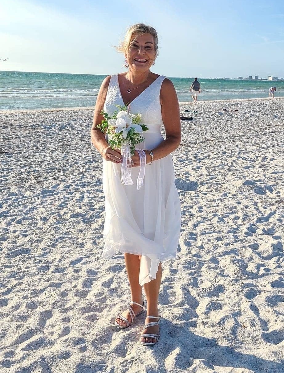 a reviewer wearing the dress in white while holding a bouquet on the beach
