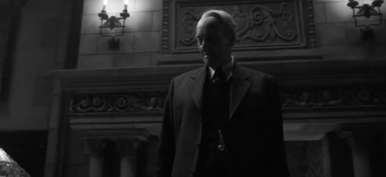 Charles Dance stood in front of a grand fireplace in Mank
