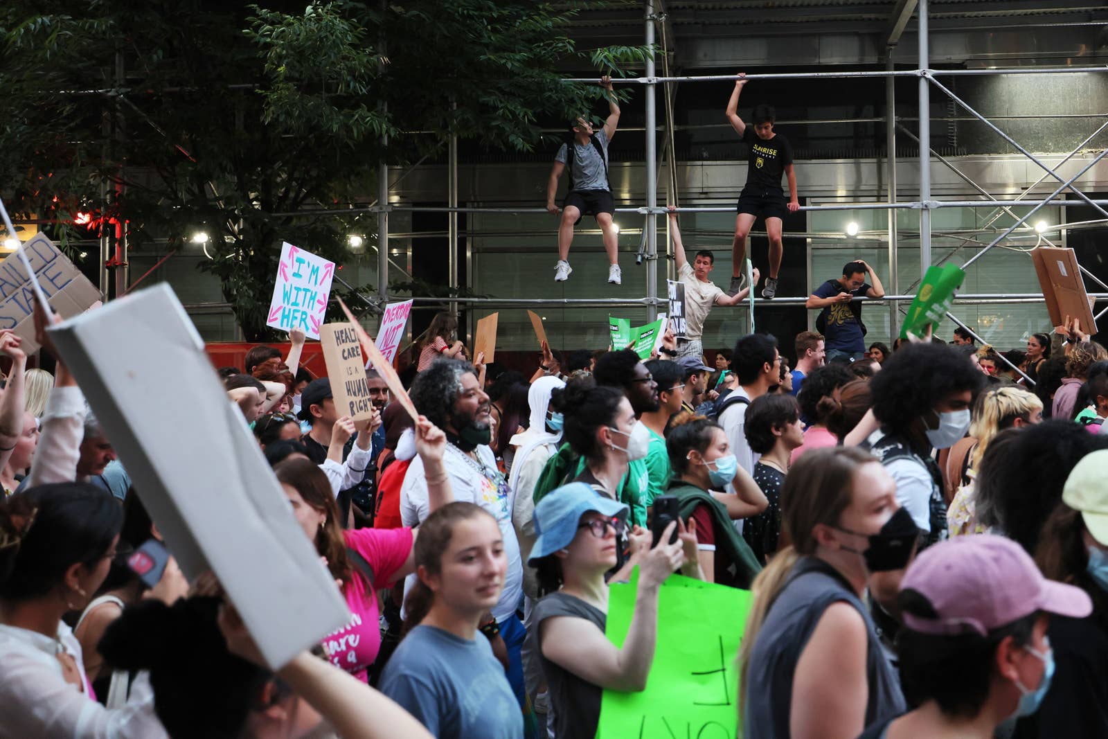A crowd of people march down the street and hold signs, some also wearing masks