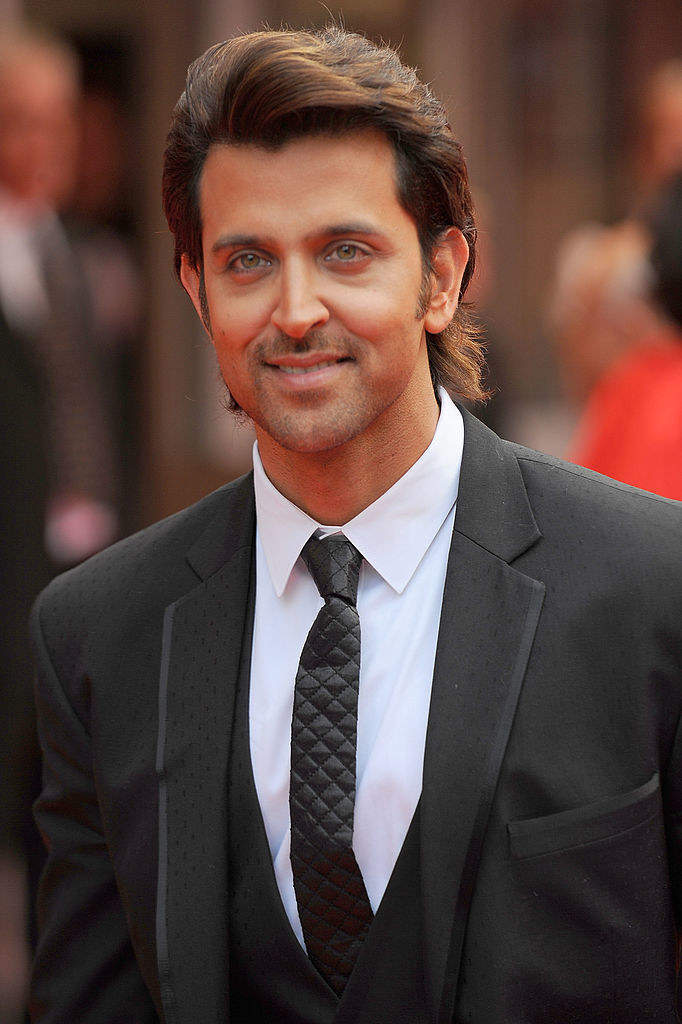Hrithik Roshan, wearing a suit and tie, smiles and poses for a picture