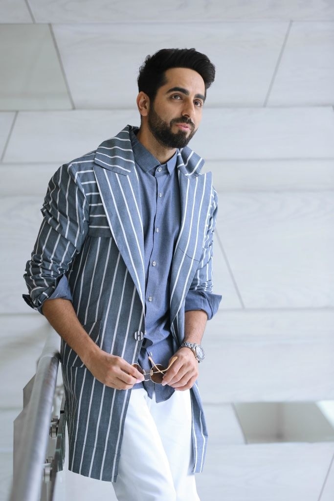Ayushmann Khurrana wearing a pinstriped jacket, poses with his sunglasses in his hands