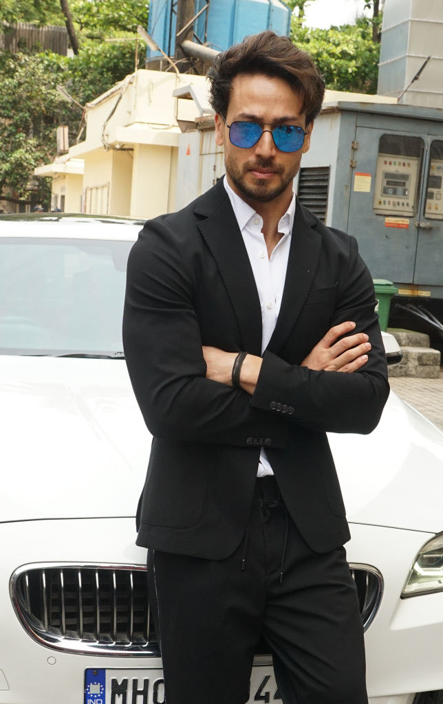 Tiger Shroff, wearing sunglasses, poses for a picture with his arms crossed