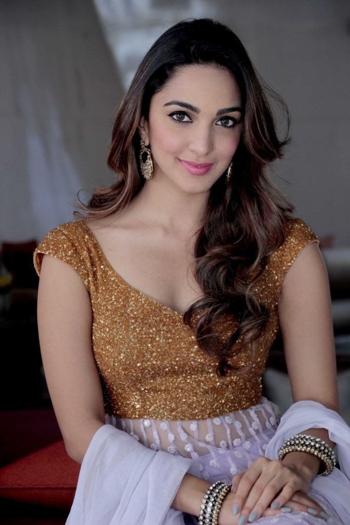Kiara Advani, wearing blingy clothes and jewellery, smiles and poses for a picture