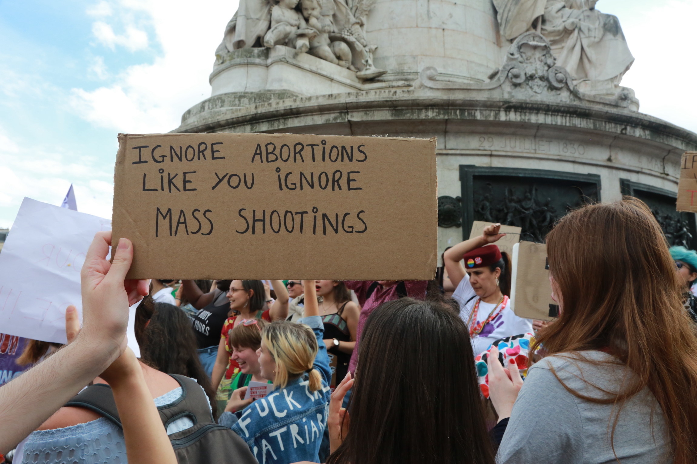 Someone holding a sign that says, &quot;Ignore abortions like you ignore mass shootings.&quot;